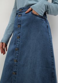 Gonna A-line in denim con lavaggio medio, chiusura anteriore con bottoni, cinque bottoni in metallo e tasche laterali. Tessuto testurizzato.