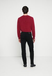 Κόκκινο μακρυμάνικο πουκάμισο με υφασμάτινο σχέδιο, συνδυασμένο με μαύρο παντελόνι στενής γραμμής και casual παπούτσια. Το φόντο είναι απλό λευκό.