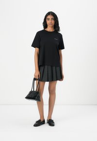 T-shirt nera in cotone con maniche corte, abbinata a una gonna grigia plissettata. Tiene una piccola borsa nera con due manici. Mocassini neri.