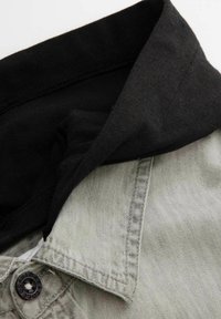 Szara i czarna koszula z kołnierzykiem, o fakturze dżinsu, z dodatkowymi guzikami i kontrastującym czarnym materiałem wewnątrz kołnierza.