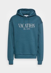 Felpa color teal con la scritta "VACATION CLUB Est. 2016" in bianco, tasca a marsupio frontale e polsini e orlo a costine. Tessuto morbido.