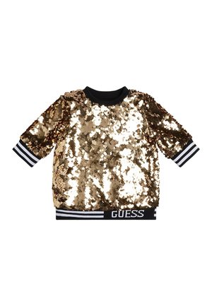 Top à manches courtes en sequins dorés avec des poignets et un ourlet rayés noirs et blancs, avec le nom de la marque Guess au bas de l'ourlet.