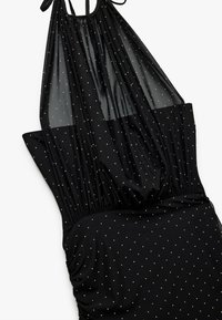 Robe noire à encolure halter avec un haut en maille froncée et un bas froncé. Décorée de petits points multicolores sur l'ensemble.