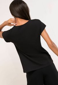 Melna īsām piedurknēm T-krekls, izgatavots no mīksta auduma, ar vienkāršu apaļu kakla izgriezumu un brīvu piegriezumu, bez redzamām rakstām vai akcentiem.