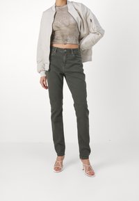 Jeans de tiro alto en verde oliva con un ajuste ceñido, combinados con una chaqueta bomber gris claro y un top gris corto. Presenta tacones blancos con tiras.