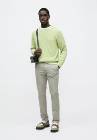 Šviesiai žalias megztinis, smėlio spalvos kelnės ir dviejų tonų batai. Juoda per petį nešiojamą rankinę su sidabro spalvos apvadais. Paprastas fonas.