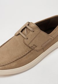 Pantofii de plajă din suede bej au o textură netedă, vârf rotund și talpă din cauciuc bej contrasting. Au șireturi și accente decorative de cusătură.
