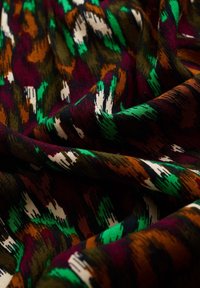 Vävt tyg med ett livfullt, flerfärgat mönster med mörkgrön, bourgogne, orange och vita accenter. Mjuk textur med en subtil glans.