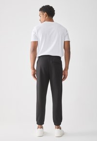 Sorte joggere med elastisk midje og mansjetter, en liten baklomme detalj, parret med en ensfarget hvit t-skjorte og hvite joggesko.