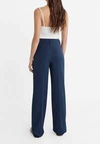 Pantalons larges bleu marine avec une texture lisse et une taille haute. Présente des pinces avant et une ceinture ajustée. Design simple et élégant.