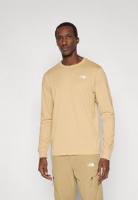 Μπεζ μακρυμάνικο t-shirt από βαμβάκι, με μικρό λευκό λογότυπο The North Face στο αριστερό στήθος, στρογγυλή λαιμόκοψη και κανονική εφαρμογή.