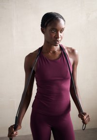 Burgundyröd träningslinne med en åtsittande design, tillverkat av elastiskt material, tillsammans med matchande leggings och ett svart hopprep.