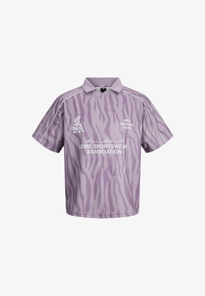 Violeta īss piedurkņu sporta krekls ar zebras svītrām, baltu apdari uz piedurknēm un baltu tekstu "Core Sportswear Association" un "World Performance Studio".