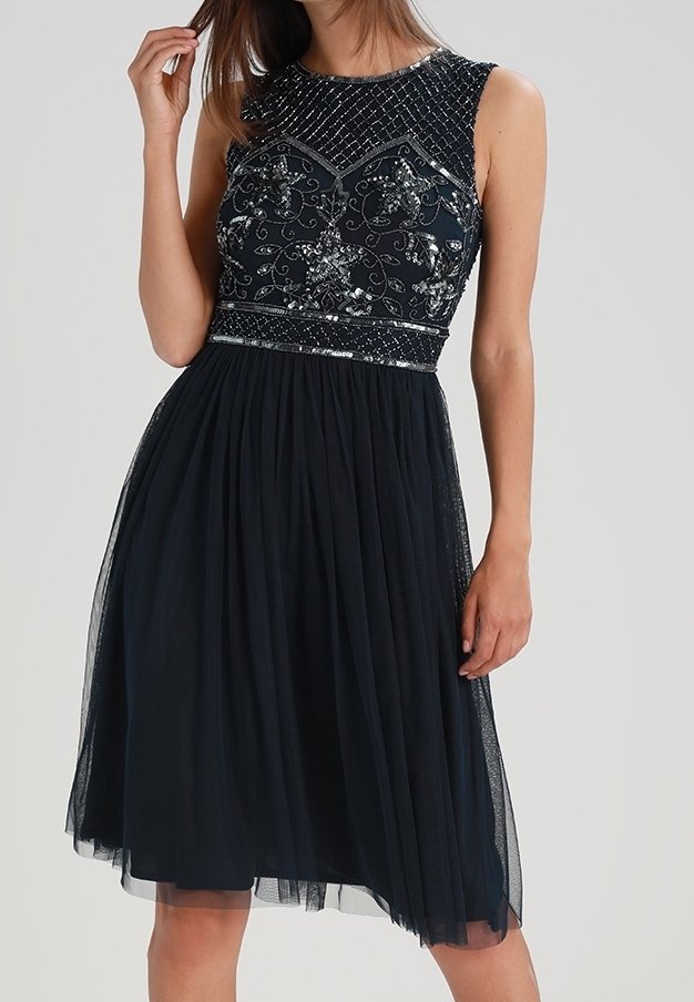 Mörkblå klänning med en figursydd bodice med pärl- och paljettdekorationer, en utställd tylskirt och en rund halsringning.