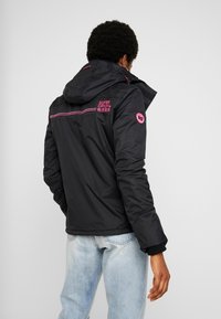 Schwarze isolierte Jacke mit Kapuze, die pinke Akzente und ein Logo auf dem Rücken hat. Strukturiertes Material und elastische Bündchen zur Anpassung.