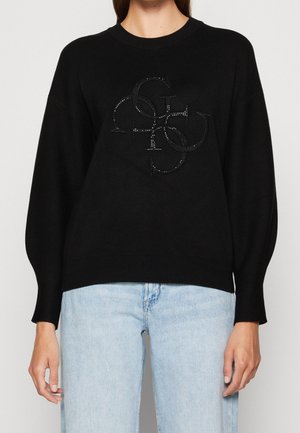 Black long-sleeve sweater with textured overlapping capital letters design on chest, worn with light blue jeans against plain background.