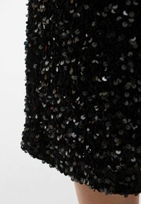 Tissu noir à sequins avec une surface dense et texturée. Les sequins sont circulaires et brillants, créant une apparence réfléchissante.