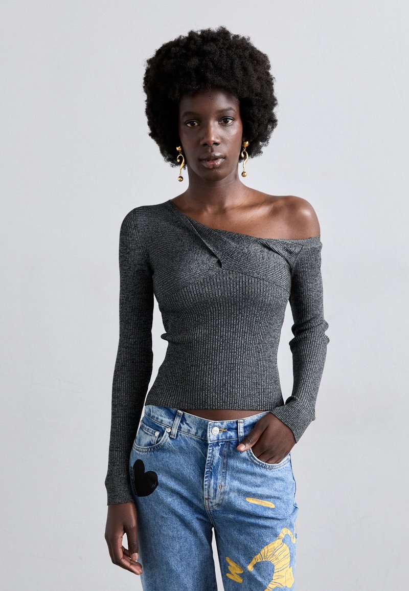 Γκρι ριχτό τοπ μακρυμάνικο με σχέδιο off-shoulder, σε συνδυασμό με μπλε τζιν παντελόνι που διαθέτει κίτρινες και μαύρες λεκέδες μπογιάς.