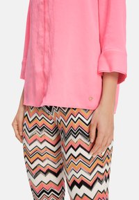 Helles pinkes Hemd mit umgeschlagenen Ärmeln, kombiniert mit legging im mehrfarbigen Zickzack-Muster in Pink, Schwarz und Weiß.