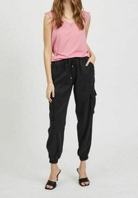 Rosa ärmlös topp med spetsdetalj, kombinerad med svarta cargobyxor med elastiska muddar och fickor, bärs med svarta öppna klackar.