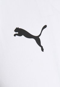 Logo de Puma negro sobre un fondo de tela blanca, que representa la silueta de un gato saltando con curvas suaves y sin adornos adicionales.