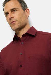 Bordeaux knoopshirt met gestructureerde kraag, zwarte knopen en een borstzak links met een klein geborduurd detail.
