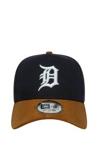 Zwarte pet met een bruine suède klep, met een geborduurd wit "D"-logo aan de voorkant. Verstelbare maat met een ronde zwarte label op de klep.