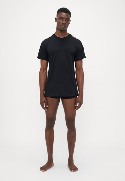 Svart t-shirt med kort ärm i bomull, med rundad halsringning, som har texturerade detaljer på axlarna och en diskret logotyp.
