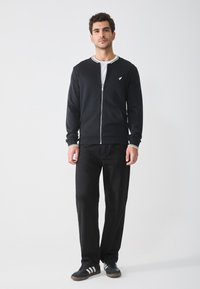 Black zip-up jacket with white and black striped collar, paired with black pants and dark sneakers featuring white stripes. Letting detailed design show.