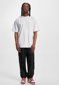 Weißes, übergroßes Baumwoll-T-Shirt mit kurzen Ärmeln, kombiniert mit schwarzen Cargo-Hosen mit Taschen und roten Sneakers mit weißen Akzenten.
