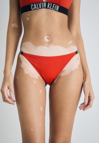Ensemble de bikini rouge comprenant un haut triangulaire avec une bande noire et un bas taille basse assorti. Tissu lisse et extensible sans motifs visibles.