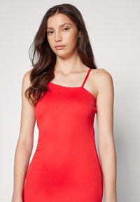 Robe rouge ajustée en tissu lisse, dotée de fines bretelles réglables et d'un col rond subtil. La structure épouse étroitement le corps.