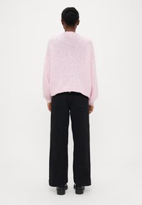 Ροζ πλεκτό πουλόβερ με άνετη εφαρμογή, ριμπ τελείωμα και μακριά μανίκια, σε συνδυασμό με μαύρο παντελόνι φαρδιάς γραμμής και μαύρα παπούτσια.