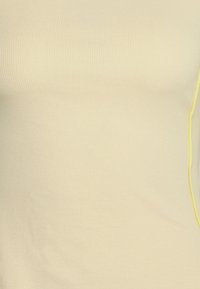 Raitapinta keltainen hihaton paita, jossa on tiukka muotoilu ja joustava kangas. Yhdellä sivulla on erottuva keltainen tikkaus.