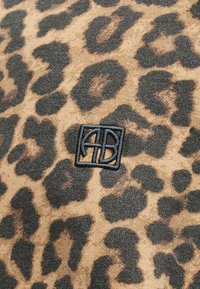 Ύφασμα με λεοπάρ μοτίβο και μαύρα κεντημένα γεωμετρικά αρχικά «AB» στο κέντρο μέσα σε περίγραμμα τετραγώνου.