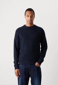Navy ribbed sweater with a round neck, long sleeves, and a textured knit pattern, paired with dark blue jeans.
