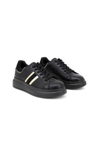 Pair of black leather sneakers with black laces, thick soles, and two beige side stripes with mesh detail.