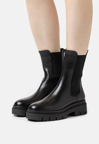 Botas de tobillo de cuero negro con paneles laterales elásticos y una suela de goma gruesa. Textura suave con detalles de costura mínimos.