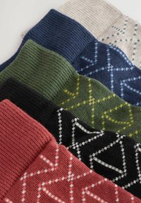 Chaussettes tricotées multicolores disposées en pile, présentant des motifs géométriques dans des teintes de marine, vert, rouge, noir et crème.