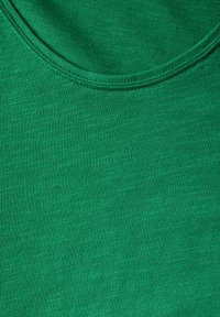 Zelený textilní top s kulatým výstřihem, hladkou strukturou a jemným melírováním. Měkký a elastický materiál vhodný pro běžné nošení.