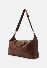 Sac de voyage en cuir marron avec une texture lisse, une forme incurvée, des poignées doubles et une sangle ajustable. Doté d'une fermeture éclair et d'accents en métal.