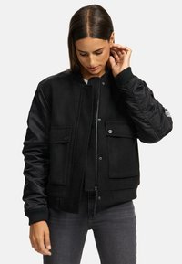 Black bomber jacket featuring a wool body and quilted nylon sleeves, front pockets, ribbed cuffs, and a zipper closure.