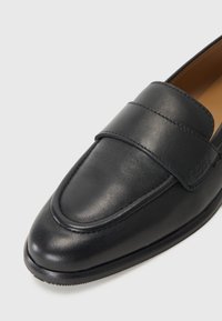 Černé kožené mokasíny s hladkým povrchem, které mají široký svrchní pás a decentní branding. Design zahrnuje kulatou špičku a šité detaily.