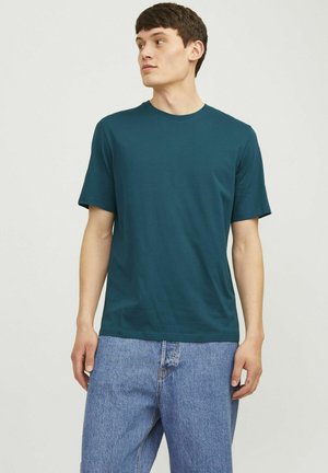 Teal crew-neck t-shirt made of soft cotton. Features short sleeves and a relaxed fit. Paired with light blue, loose-fitting jeans.