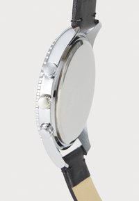 Carcasă de ceas din oțel inoxidabil argintie, rotundă, cu trei butoane, curea din piele neagră, bezel texturat și spate de carcasă neted și reflectorizant.