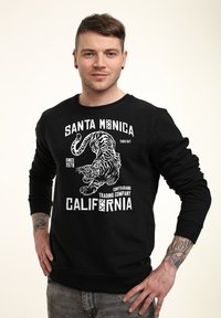 Černá mikina s kulatým výstřihem má na přední straně grafiku bílé tygra a nápisy "SANTA MONICA", "TIGER BAY" a "CALIFORNIA".
