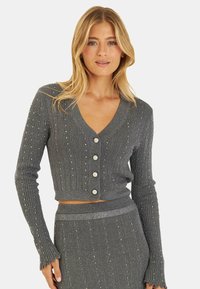 Grau gerippter Cardigan mit langen Ärmeln und V-Ausschnitt, ausgestattet mit dekorativen Knöpfen und verziert mit kleinen Perlen. Texturierte Oberfläche.