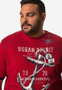 Camiseta de algodón roja con gráficos de temática náutica, que incluyen un ancla y una brújula, con el texto "Espíritu Oceánico" y "Aventura Oceánica."
