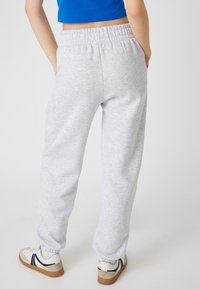 Lichtgrijze sweatpants met een zachte textuur, elastische tailleband en taps toelopende boorden. Draagt met witte sneakers met zwarte accenten.