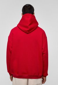 Rode hoodie met een grote, zachte capuchon en verlaagde schouders. Ribgebreide manchetten en zoom, met een gladde, textuurachtige stofafwerking.